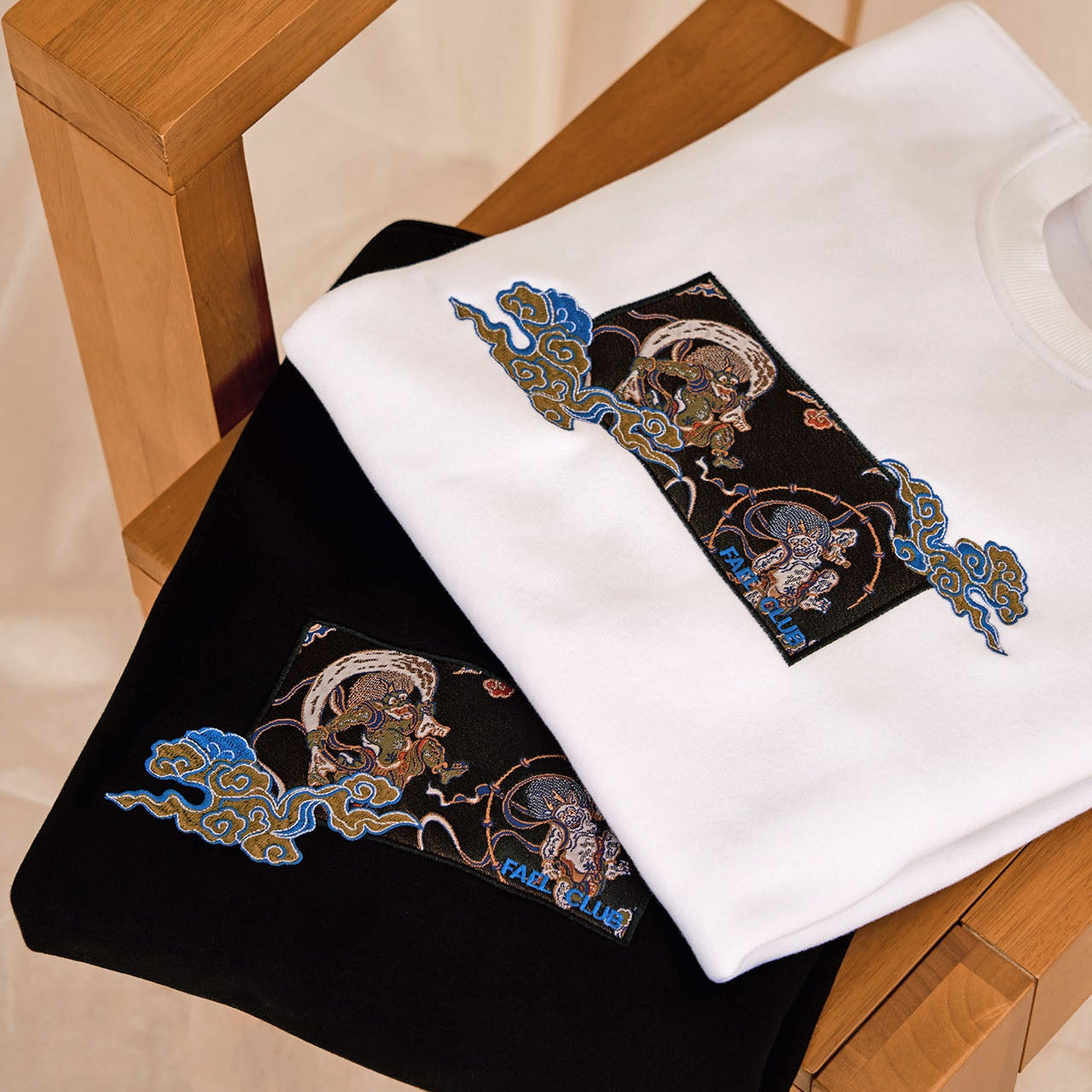 Embroidered Fujin and Raijin on black and white sweatshirt on a wooden chair